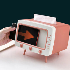Pink and white retro TV-shaped tissue box holder with a hand inserting a phone and a tissue on top