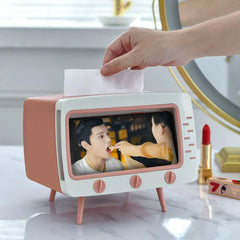 Hand pulling a tissue from a retro TV-shaped tissue box holder with a drama scene displayed in its front frame