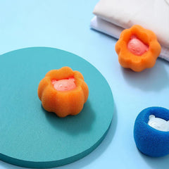 Una bola de lavandería naranja con forma de flor sobre un círculo verde azulado; bolas de lavandería naranjas y azules a juego están al fondo.