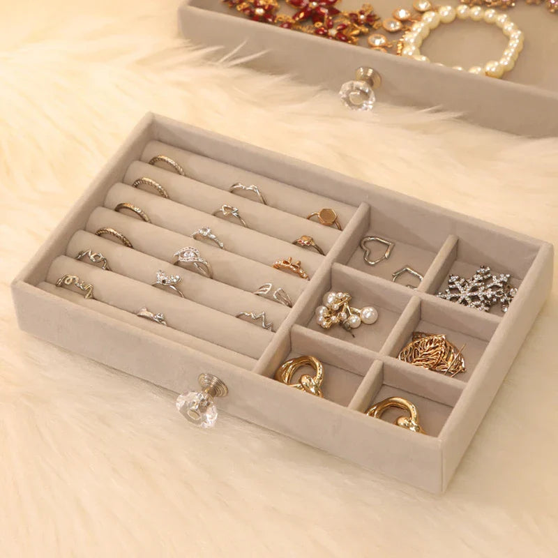 Close-up of a beige ring necklace earring display storage box tray with slots for rings and small compartments for earrings, holding jewelry.