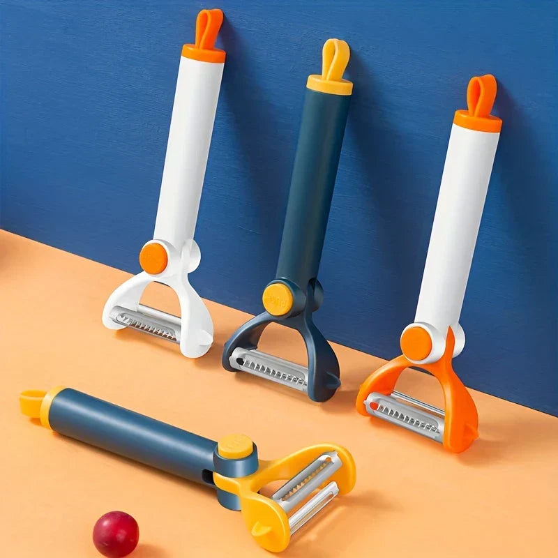 Pelador de verduras: cuatro peladores multicolor de doble hoja, tres de pie y uno acostado, sobre una superficie naranja contra una pared azul, con una pequeña fruta roja cerca