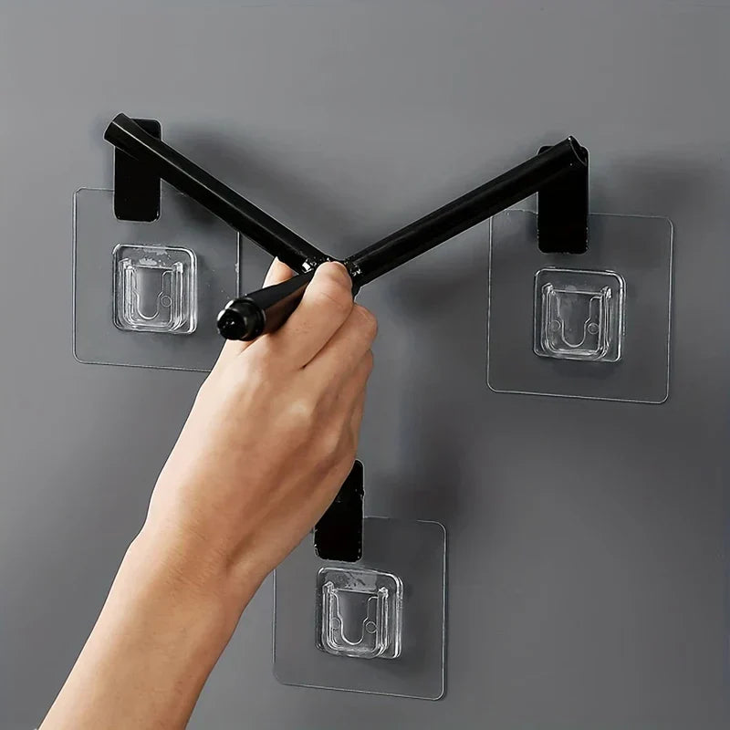 Reisspender - Hand positioniert ein schwarzes Stativbein gegen wandmontierte transparente Klebehaken, verwendet zur Montage eines Reisspenders