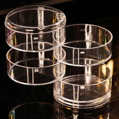 Four empty clear round tiered containers of a jewelry organizer box stacked in staggered arrangement against a dark reflective surface