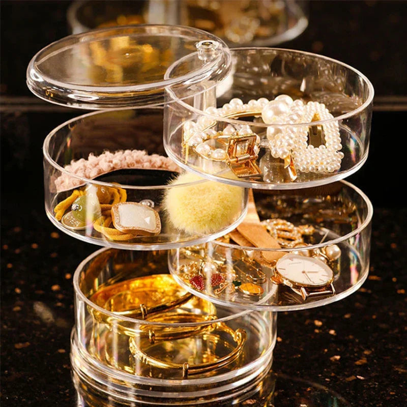 4-layer rotating clear jewelry organizer box partially fanned open, holding bracelets, watches, hair clips, and assorted jewelry on a dark surface