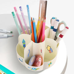 Cream 360° rotating makeup brush holder with space-themed stickers, filled with pens, pencils, scissors, and stationery, placed on a white desk