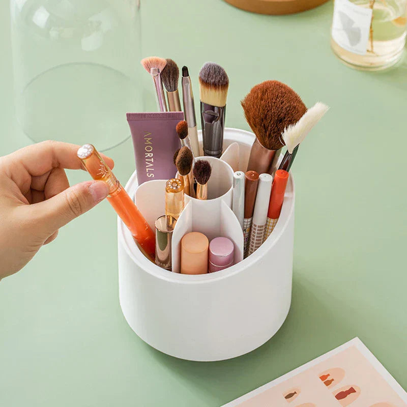 Hand takes a lip product from a white rotating makeup brush holder holding brushes, pens, and cosmetic tubes on a green table.