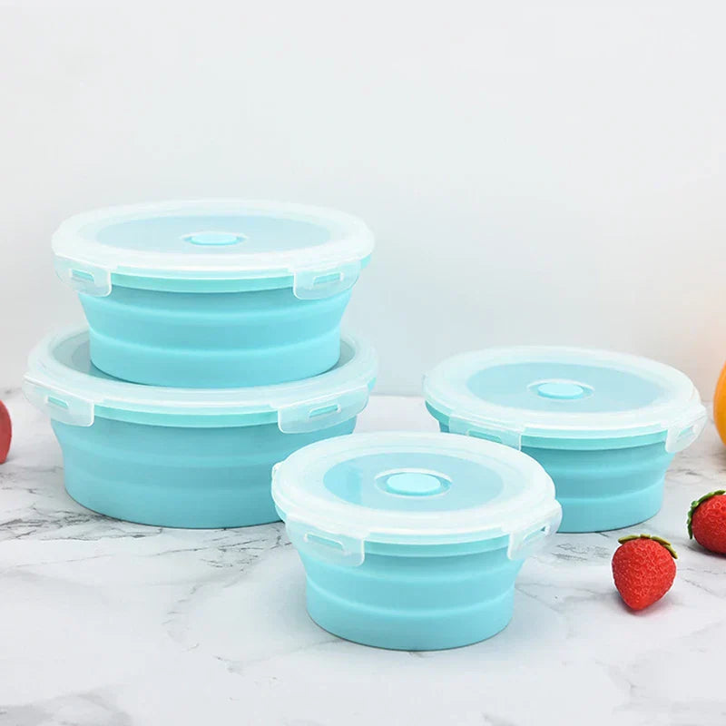 Four teal collapsible food storage container set with lids, two stacked, two placed beside them on a marble surface with decorative strawberries