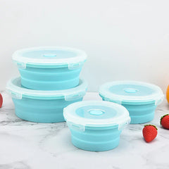 Four teal collapsible food storage container set with lids, two stacked, two placed beside them on a marble surface with decorative strawberries
