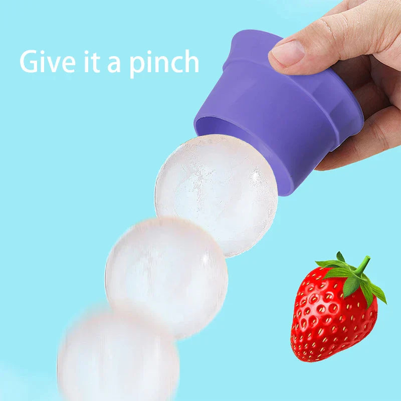 Pinching a purple ice ball maker to release round ice balls, with a strawberry beside them on light blue