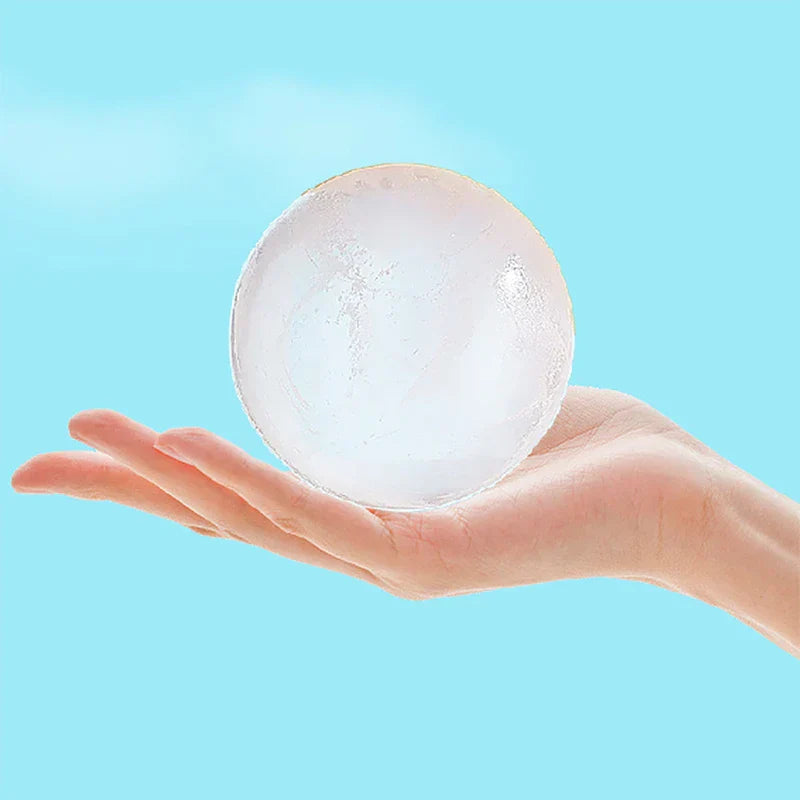 A clear round ice ball resting on an open palm, made with an ice ball maker, against light blue