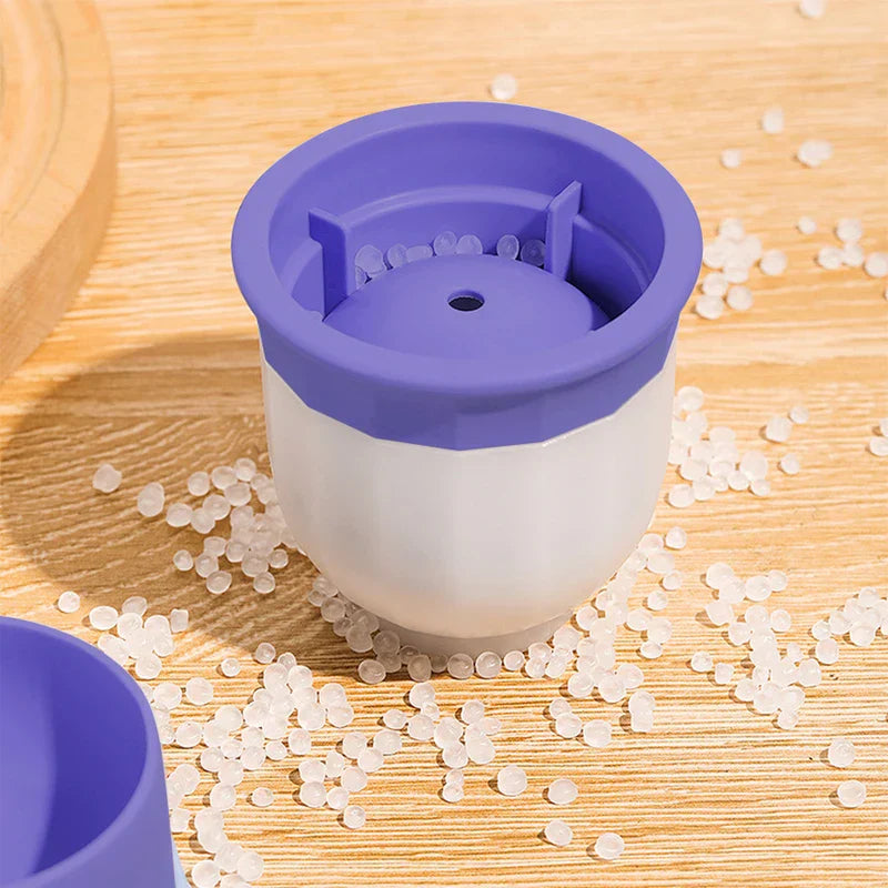 White and purple ice ball maker sits on a wooden surface surrounded by clear plastic pellets