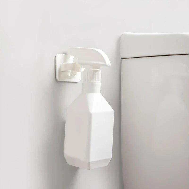 gancho de pared para colgar - gancho blanco montado en una pared blanca sosteniendo una botella de spray blanca junto a un inodoro