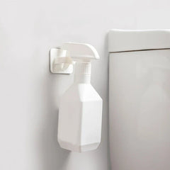 gancho de pared para colgar - gancho blanco montado en una pared blanca sosteniendo una botella de spray blanca junto a un inodoro