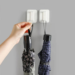 Wall Hook Hanger - Two white wall hook hangers on a gray wall holding folded umbrellas, with a hand hanging one umbrella