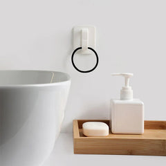 White wall hook hanger with a black circular ring towel holder mounted on a wall near a basin, soap, and pump bottle on a wooden tray