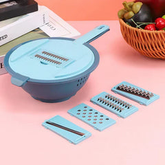 Blue vegetable slicer grater set with 4 interchangeable blades on a pink table next to a fruit basket