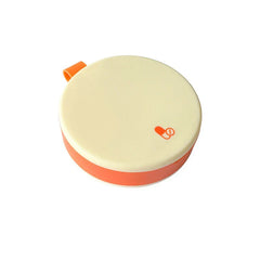Closed cream and orange round travel pill organizer box with a capsule icon on its lid, shown on a white background