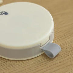 Close-up of the latch closure on a closed round travel pill organizer box resting on a light wood surface