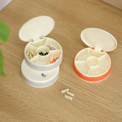 Travel Pill Organizer Box - Two open travel pill organizer boxes (gray stacked, orange) with assorted pills inside, three capsules on a wood surface.