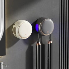 Toothbrush Sanitizer Holder - Two wall-mounted toothbrush sanitizer holders (white and dark gray) holding electric toothbrushes, one with glowing blue light, on a bathroom wall.