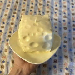 Jumbo Stress Ball - A cheese-shaped pale yellow candle with a wick sits on a small pale yellow plate held in a hand.