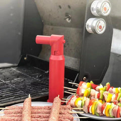 Red skewer kebab maker box stands on a grill beside plates of raw meat skewers and vegetable chicken skewers.