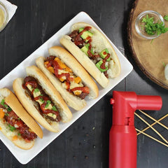 Plato con mini sándwiches armados sobre una mesa oscura junto a una caja roja de la herramienta para hacer brochetas y palillos de madera