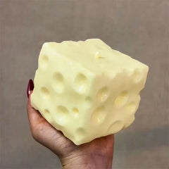 Jumbo Stress Ball - A hand with dark red nail polish holds a pale yellow cube-shaped object with multiple circular indentations across its surface.