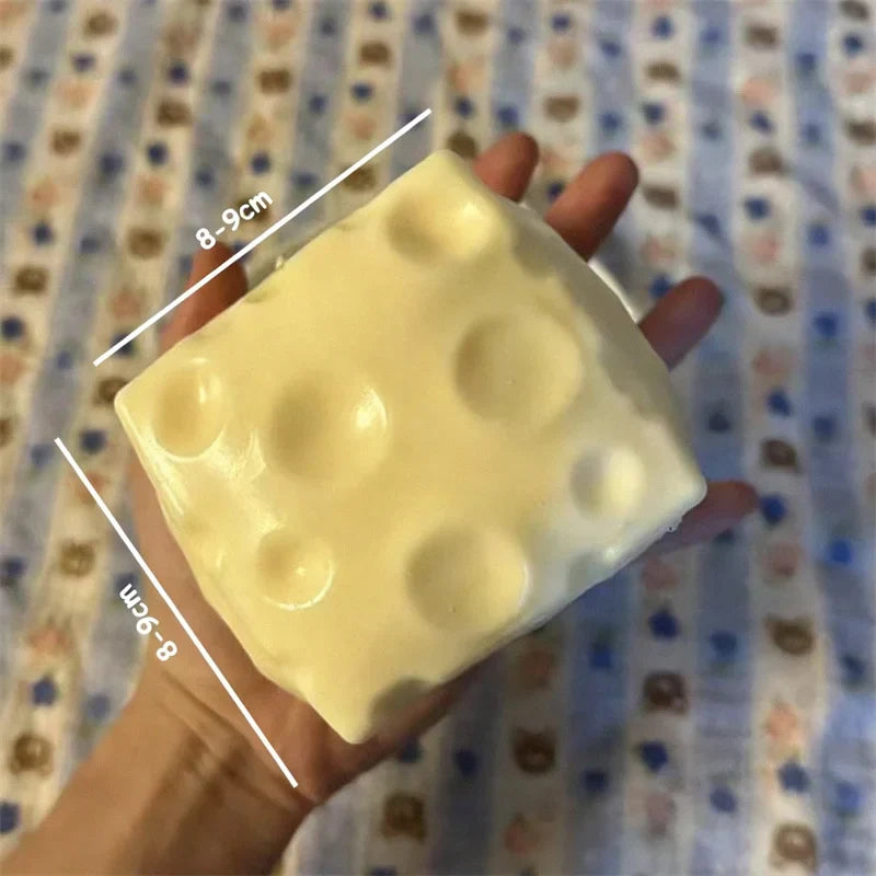 Jumbo Stress Ball - A hand holds a square, pale yellow cheese-shaped block with circular indentations, marked 8-9cm on two edges.