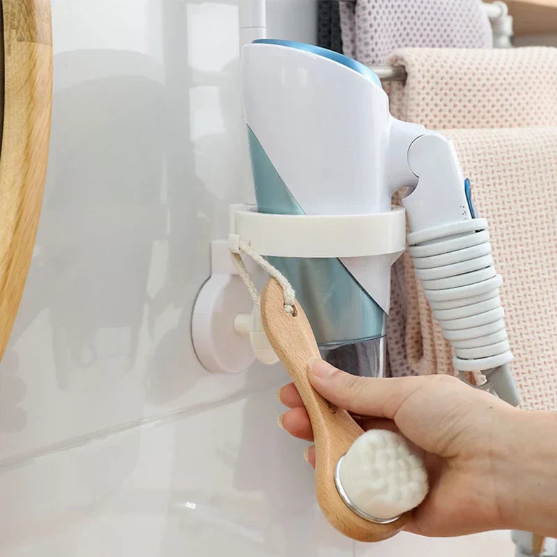 White wall-mounted towel rack with a cup holder holding a hair dryer, and a hand holding a bath brush
