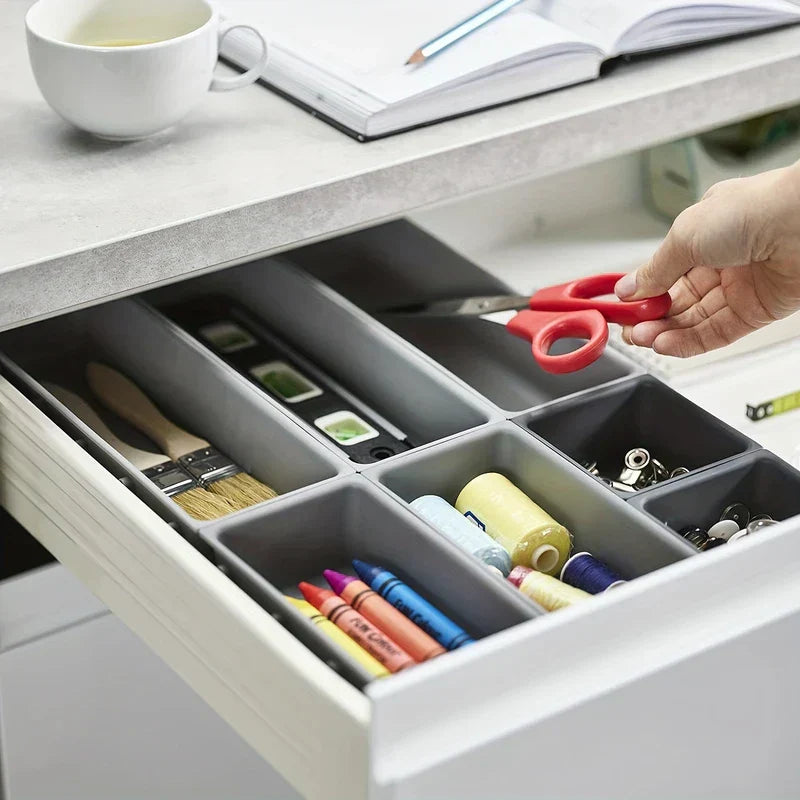 A hand reaching for scissors from interlocking storage bins organizing craft supplies inside a desk drawer