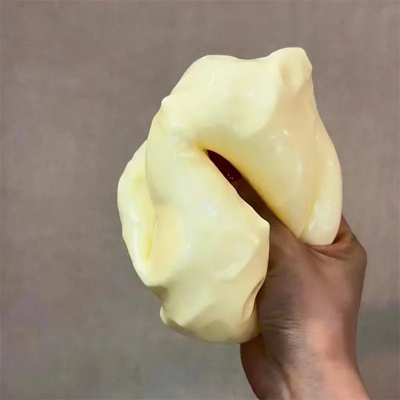 Jumbo Stress Ball - A hand squeezes a pale yellow soft cheese-shaped object, deforming it under pressure.