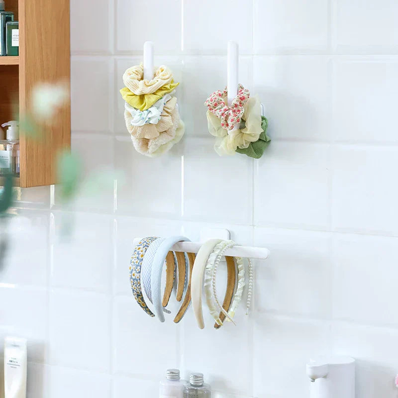 Two vertical wall hooks and one horizontal hook holding hair accessories including short hair tie items on a white tile wall