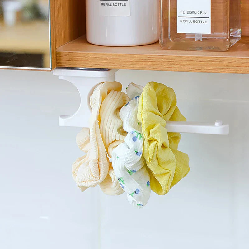 Under-shelf hook holding several scrunchies, with a short hair tie among them under a wooden cabinet shelf