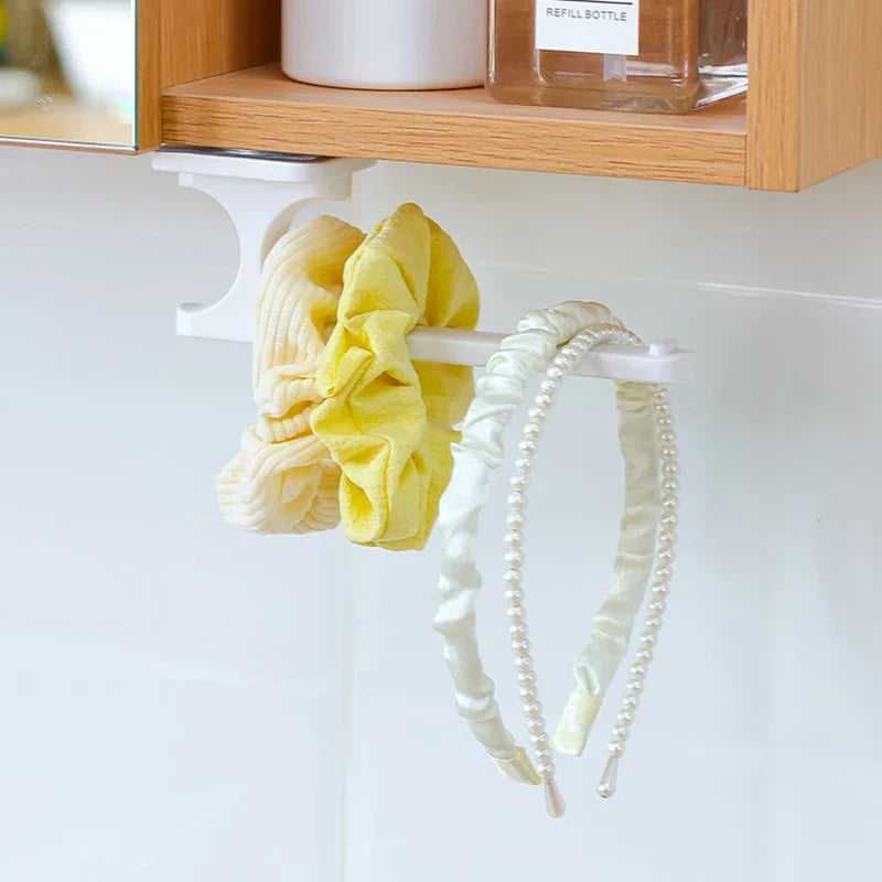 Yellow and cream short hair tie plus two pearl headbands hang from an under-cabinet white plastic hook holder.