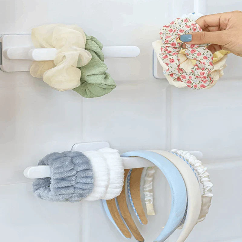 Wall-mounted adhesive hooks hold scrunchies, short hair tie items, and headbands; a hand places a floral scrunchie on one hook.