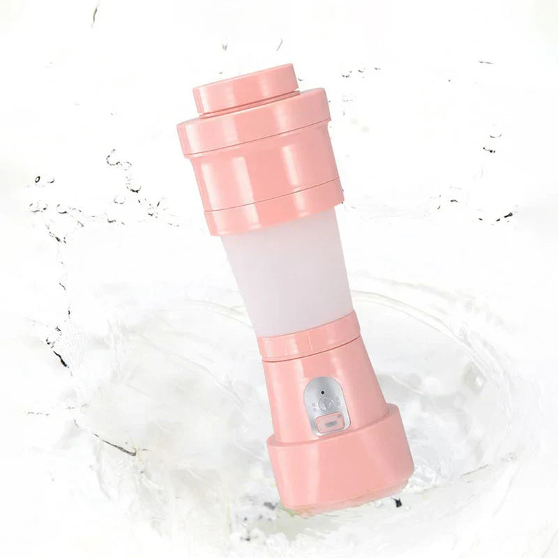 Licuadora de batidos - licuadora de batidos de una sola porción portátil de color rosa con botón de control y cuerpo translúcido, posicionada entre salpicaduras de agua blanca