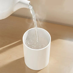 Hot water pouring from a white kettle into a white mouthwash cup holder set on a light wood surface