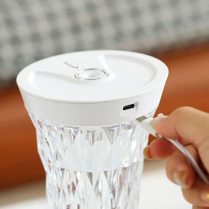 Hand inserts a USB-C charging cable into the side of a white-topped cool mist diffuser with a clear diamond-patterned body