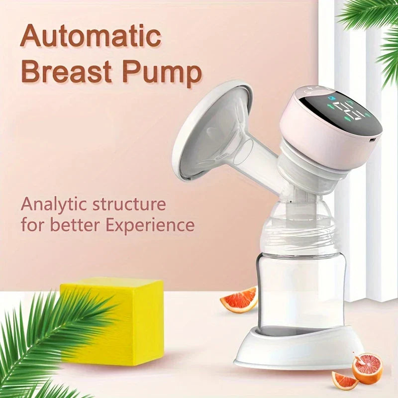 Automatic electric breast pump with clear milk bottle, displayed on light surface with decorative leaves, yellow block, and fruit slices.