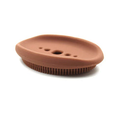 Dish Scrubber Brush - Angled view of a brown oval silicone object with raised edge, five centered top holes, and short evenly spaced bristles on its lower edge.