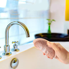 Dish Scrubber Brush - Hand holding a sudsy bristle cleaning pad next to a chrome kitchen sink faucet