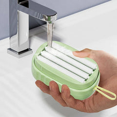 Laundry Scrub Brush - Hand holds a light green oval scrub brush under running faucet water, showing its white bristle surface.