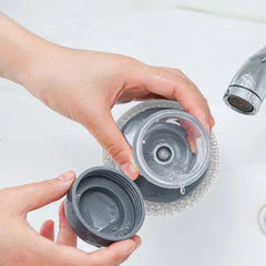 Dish Brush Soap Dispensing - Two hands unscrew the top cap of a soap-dispensing dish scrubber to open the reservoir.