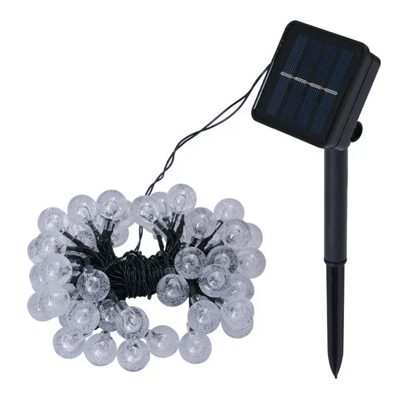 Coiled black wire bubble ball string lights next to a black stake-mounted solar panel on a white background