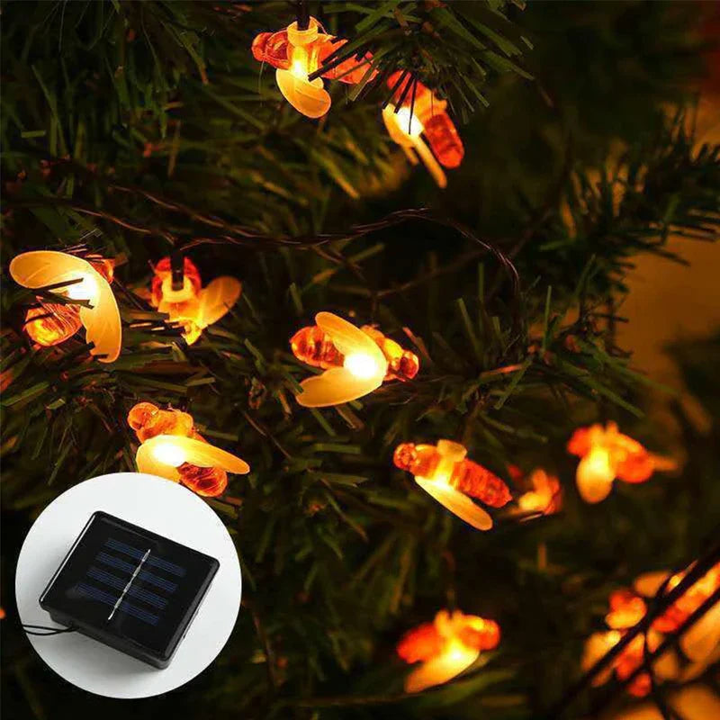 Warm glowing bee string lights wrapped in green foliage, with a solar panel inset shown in a circle.