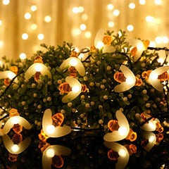 Warm glowing bee-shaped string lights draped over green leafy foliage