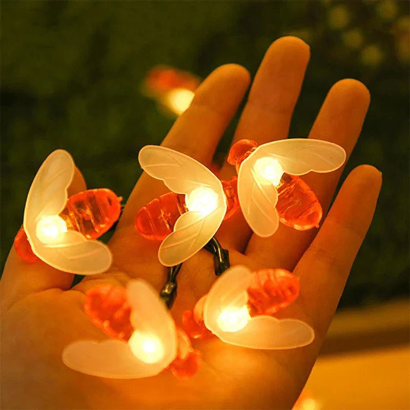 Outdoor String Lights - Close-up of a hand holding lit bee-shaped decorative string lights with translucent wings and orange bodies