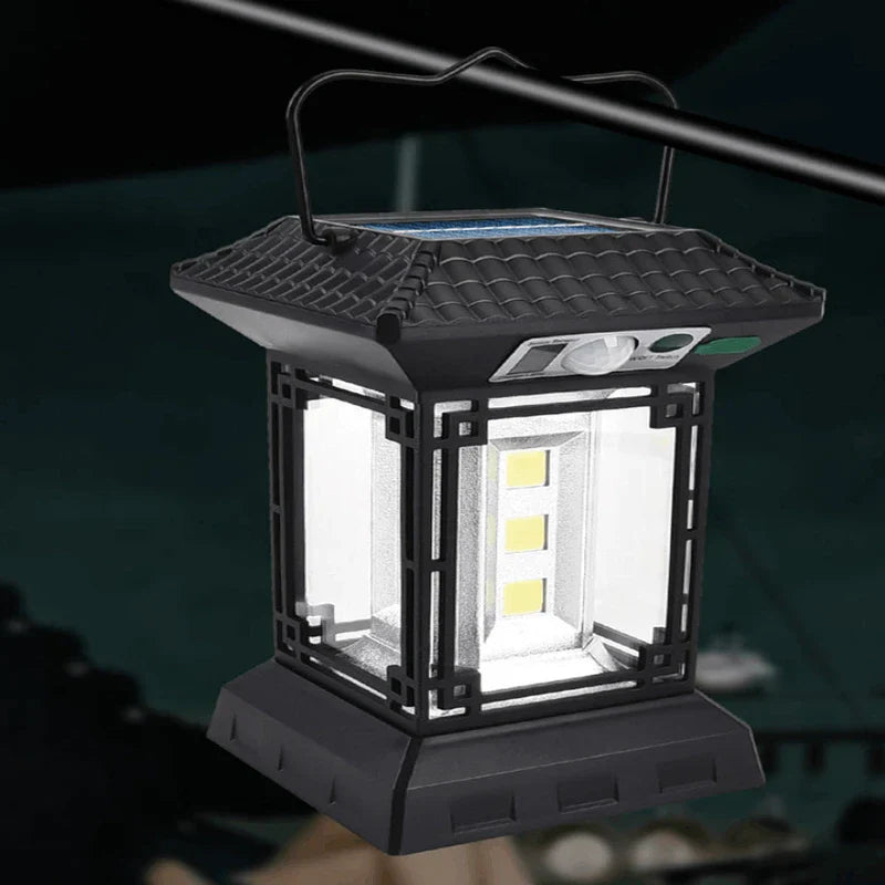 luz de campamento - Linterna negra estilo pagoda iluminada colgando de un poste metálico de tienda, elementos LED encendidos visibles a través de paneles laterales transparentes en un campamento exterior oscuro