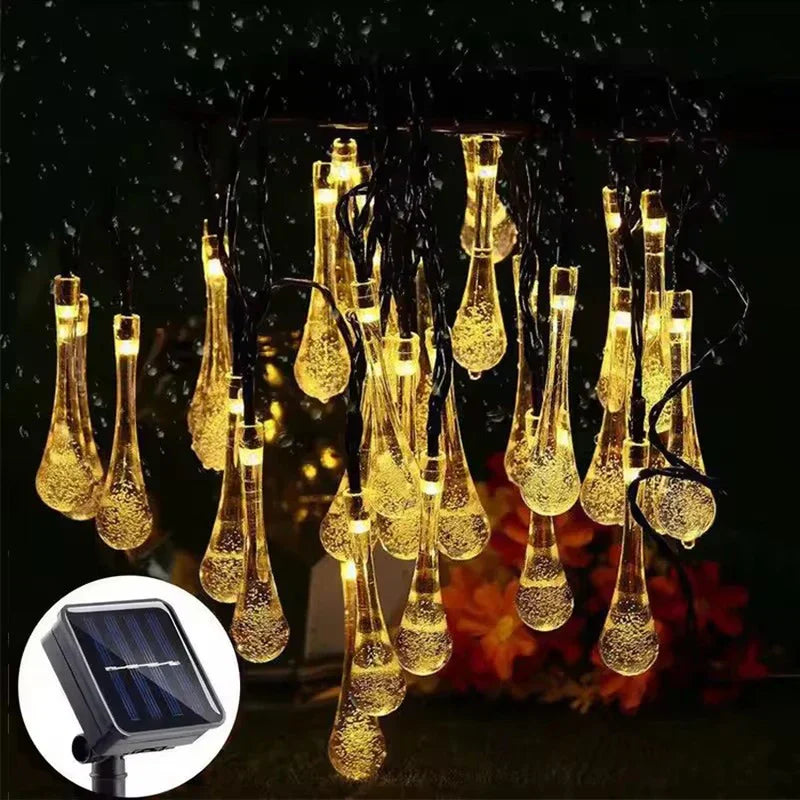 Beleuchtete Solarlichter in Wassertropfenform für den Außenbereich mit leuchtenden goldenen klaren Tropfenlampen in dunkler Regenszene, Solarpanel in kleinem kreisförmigem Einsatz